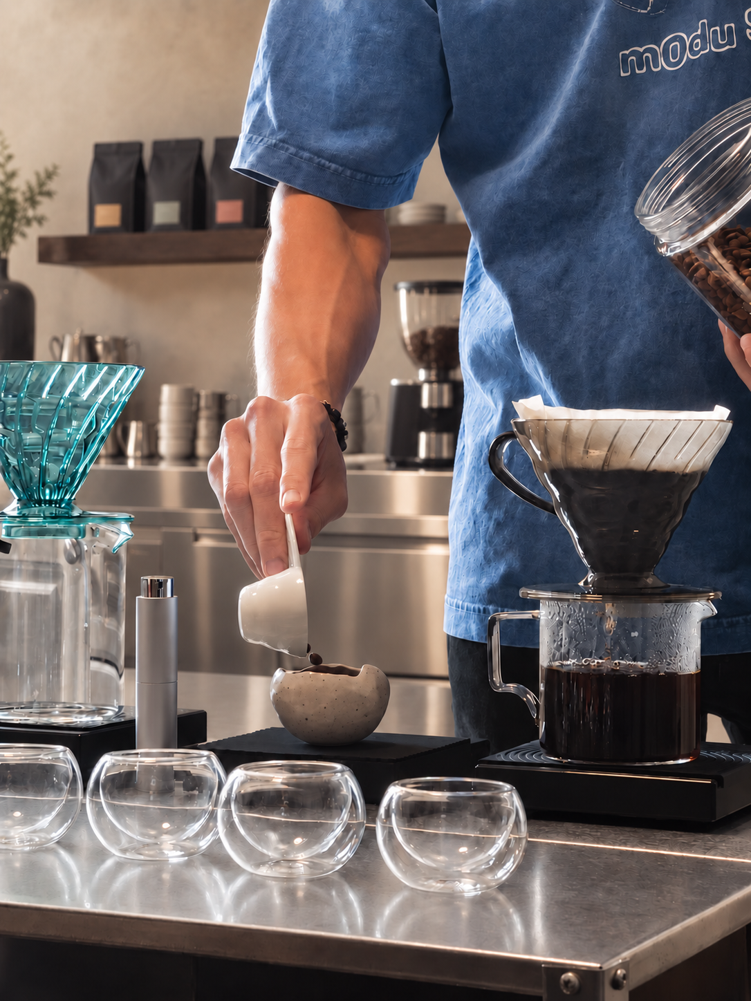 Coffee beans, V60 brewer, and tasting cups on a stainless steel bar